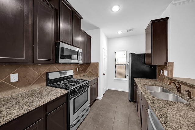 kitchen with light tile patterned flooring, appliances with stainless steel finishes, sink, dark stone countertops, and backsplash