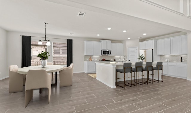 kitchen featuring white cabinetry, a kitchen breakfast bar, an island with sink, and white fridge