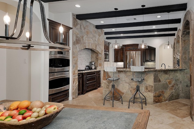 kitchen featuring a breakfast bar, stone countertops, decorative backsplash, built in appliances, and dark brown cabinetry