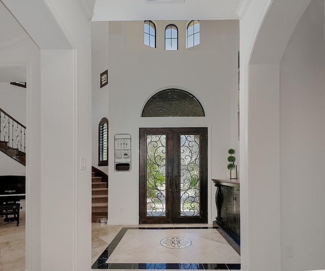 foyer entrance featuring a towering ceiling, ornamental molding, and french doors