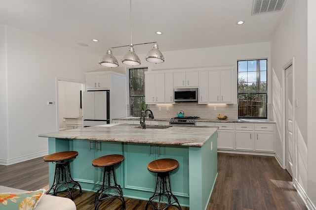 kitchen with white cabinetry, appliances with stainless steel finishes, an island with sink, and hanging light fixtures