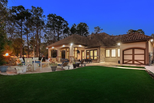 back house at dusk featuring a patio and a lawn