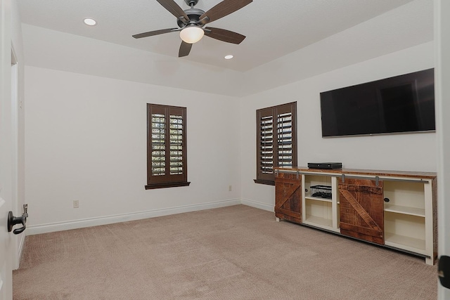 unfurnished living room featuring light carpet, ceiling fan, a tray ceiling, and a healthy amount of sunlight