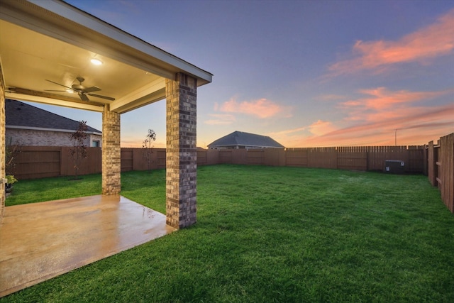 yard at dusk featuring ceiling fan and a patio area