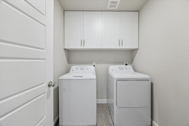 washroom featuring cabinets, washer and clothes dryer, and light hardwood / wood-style flooring