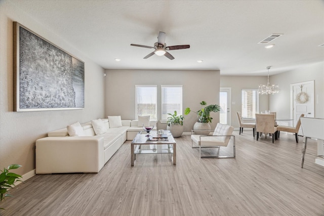 living room featuring ceiling fan with notable chandelier, a wealth of natural light, and light wood-type flooring