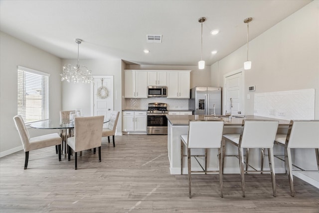 kitchen with white cabinetry, hanging light fixtures, a kitchen bar, and appliances with stainless steel finishes