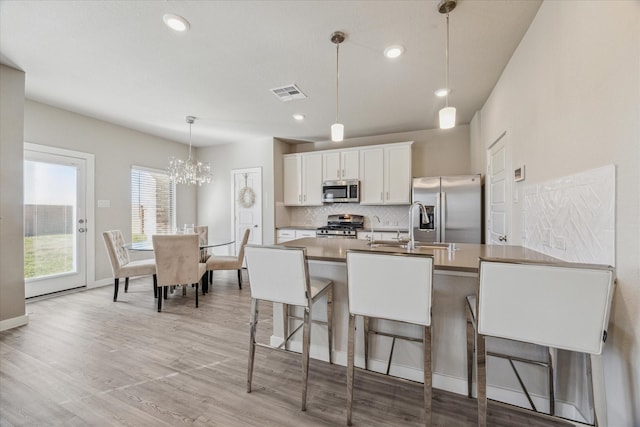 kitchen with white cabinetry, appliances with stainless steel finishes, a kitchen breakfast bar, an island with sink, and pendant lighting