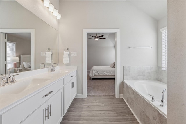 bathroom featuring lofted ceiling, hardwood / wood-style flooring, ceiling fan, vanity, and a relaxing tiled tub