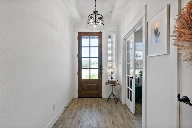 doorway featuring french doors, crown molding, an inviting chandelier, and light hardwood / wood-style flooring