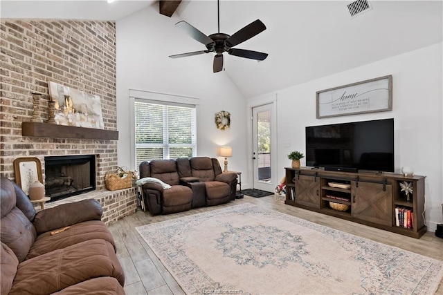 living room with a brick fireplace, beam ceiling, high vaulted ceiling, and light wood-type flooring