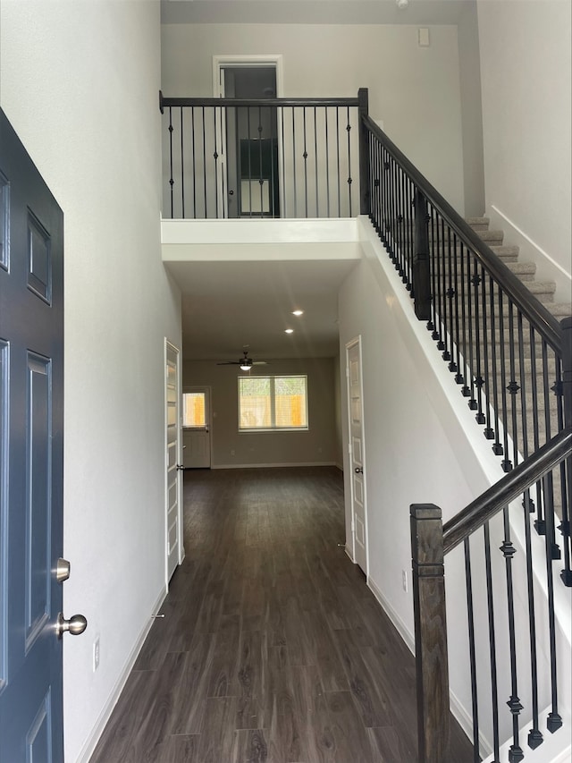 foyer featuring a towering ceiling, a ceiling fan, baseboards, and dark wood-type flooring