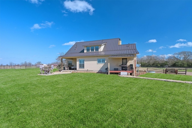 back of house with a patio, a lawn, and a rural view