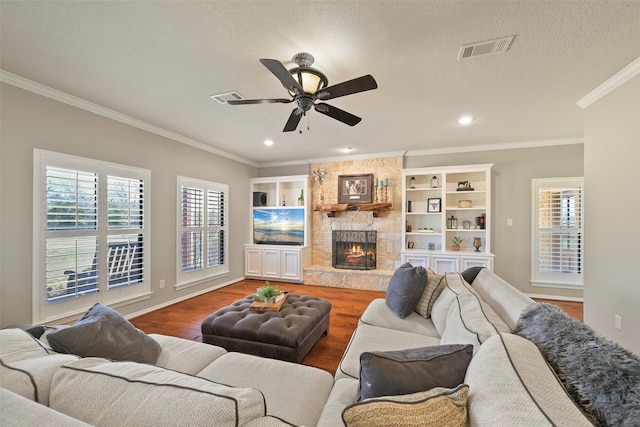 living room with a stone fireplace, wood-type flooring, ceiling fan, crown molding, and a textured ceiling