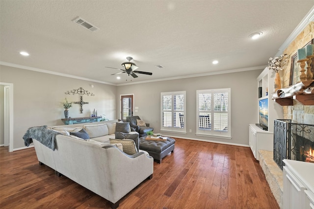 living room with dark wood-type flooring, a stone fireplace, crown molding, a textured ceiling, and ceiling fan