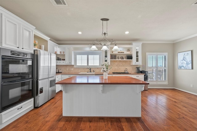 kitchen with butcher block countertops, stainless steel fridge, a center island, white cabinets, and decorative light fixtures