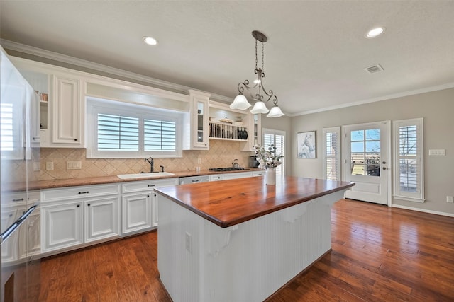 kitchen with sink, butcher block counters, white cabinets, a kitchen island, and decorative light fixtures