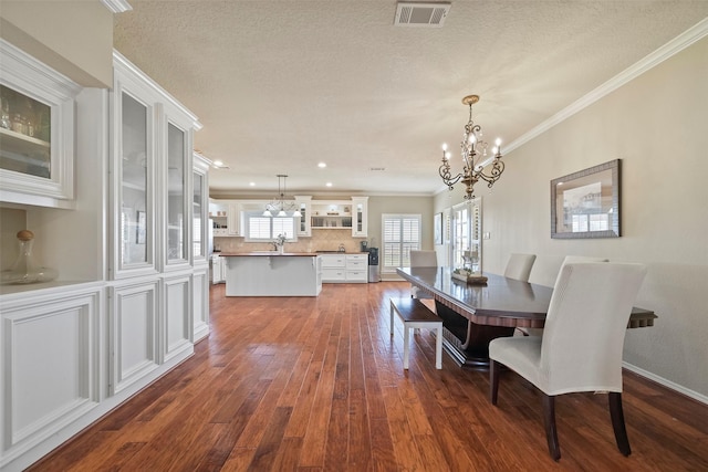 dining space with dark wood-type flooring, ornamental molding, a chandelier, and sink