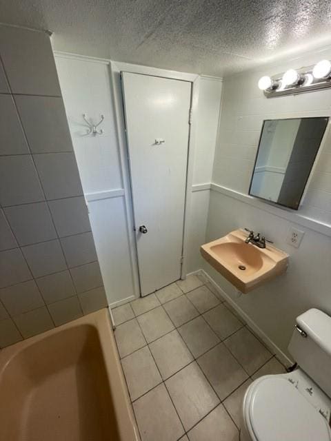 bathroom featuring sink, a bathtub, a textured ceiling, tile patterned floors, and toilet