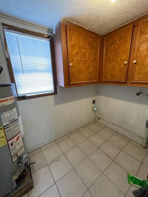 washroom featuring cabinets, a textured ceiling, light tile patterned floors, electric dryer hookup, and water heater