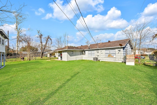 rear view of house with central AC unit and a lawn