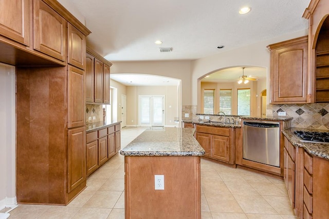 kitchen featuring sink, a center island, light tile patterned floors, light stone counters, and stainless steel appliances