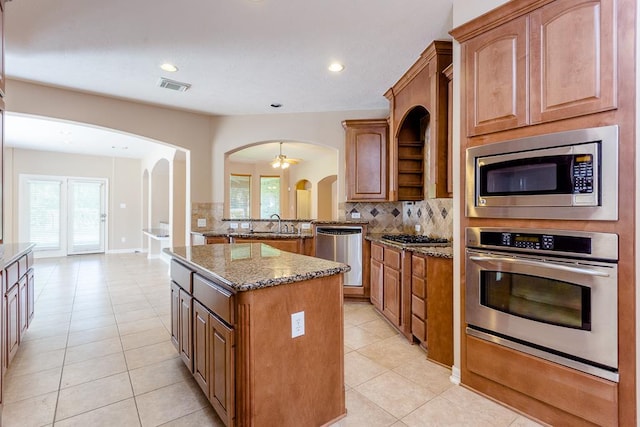 kitchen with stainless steel appliances, a kitchen island, stone countertops, and backsplash