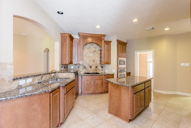 kitchen with sink, tasteful backsplash, appliances with stainless steel finishes, kitchen peninsula, and stone counters