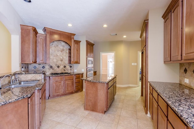 kitchen featuring sink, light tile patterned floors, dark stone countertops, appliances with stainless steel finishes, and a kitchen island