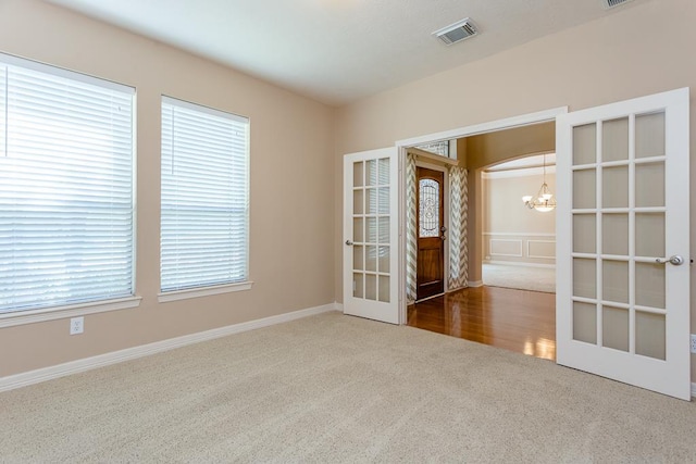 carpeted spare room with french doors and a chandelier