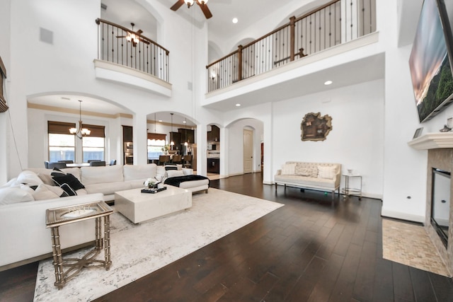 living room with ceiling fan with notable chandelier, dark wood-type flooring, and a towering ceiling