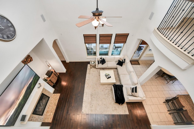 living room with a towering ceiling, dark wood-type flooring, and ceiling fan