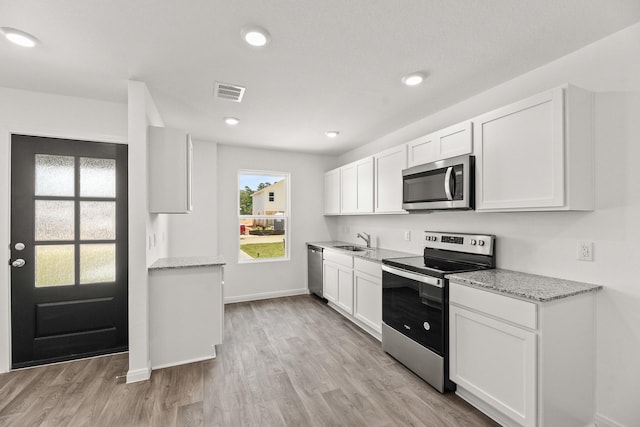 kitchen featuring appliances with stainless steel finishes, light stone countertops, light hardwood / wood-style flooring, and white cabinets