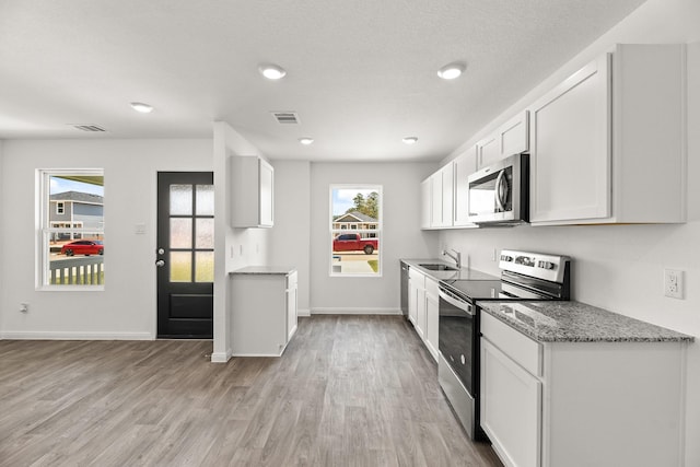 kitchen with light stone counters, light wood-type flooring, white cabinets, and appliances with stainless steel finishes