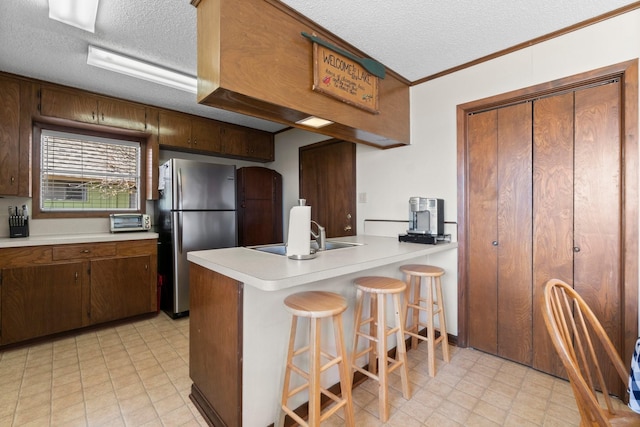 kitchen with a kitchen bar, sink, a textured ceiling, stainless steel fridge, and kitchen peninsula