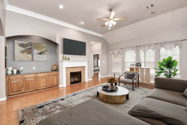 living room featuring ornamental molding, lofted ceiling, a tile fireplace, and light hardwood / wood-style flooring