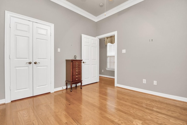 unfurnished bedroom with light wood-type flooring, baseboards, a closet, and crown molding