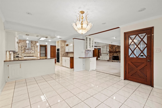 kitchen featuring hanging light fixtures, white cabinets, decorative backsplash, kitchen peninsula, and wall chimney exhaust hood