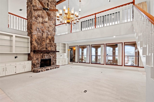 unfurnished living room with light colored carpet, a stone fireplace, a chandelier, and a towering ceiling