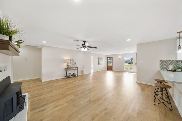 living room featuring ceiling fan, light hardwood / wood-style floors, and a wood stove