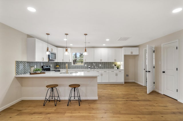 kitchen with sink, white cabinetry, hanging light fixtures, stainless steel appliances, and kitchen peninsula