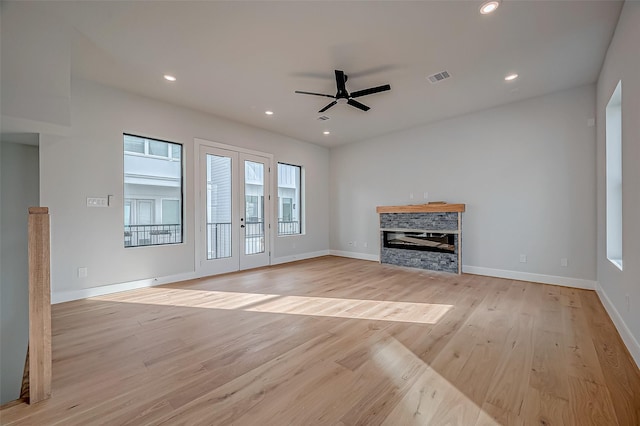 unfurnished living room featuring a fireplace, french doors, ceiling fan, and light wood-type flooring