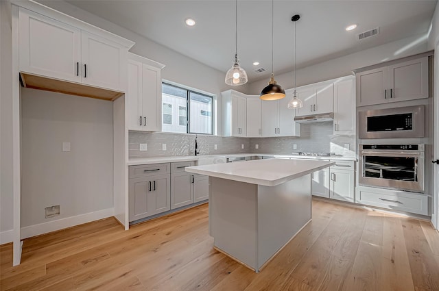 kitchen with white cabinetry, hanging light fixtures, appliances with stainless steel finishes, a kitchen island, and backsplash