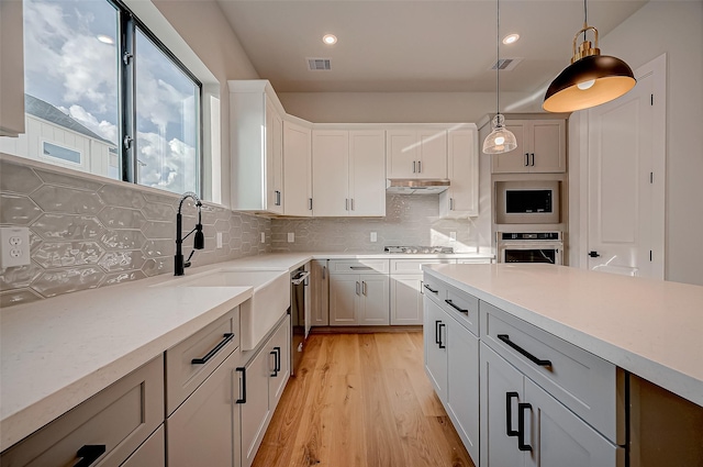 kitchen with tasteful backsplash, white cabinetry, hanging light fixtures, stainless steel appliances, and light wood-type flooring