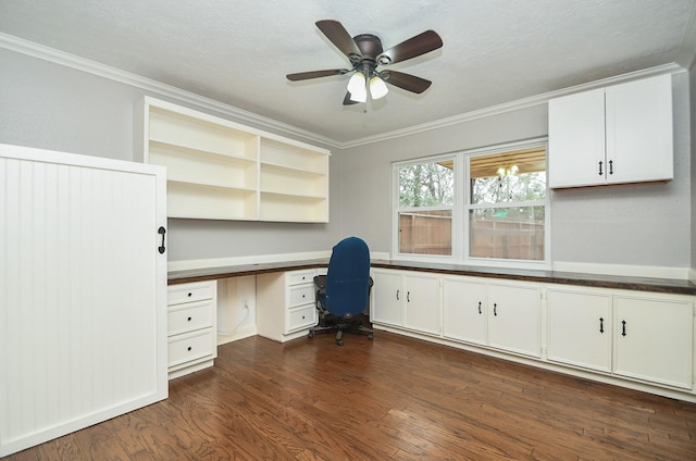 unfurnished office with ornamental molding, ceiling fan, built in desk, and dark wood-style flooring