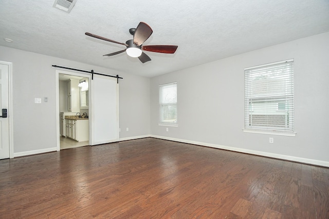 unfurnished room with dark wood-style flooring, visible vents, a barn door, a textured ceiling, and baseboards