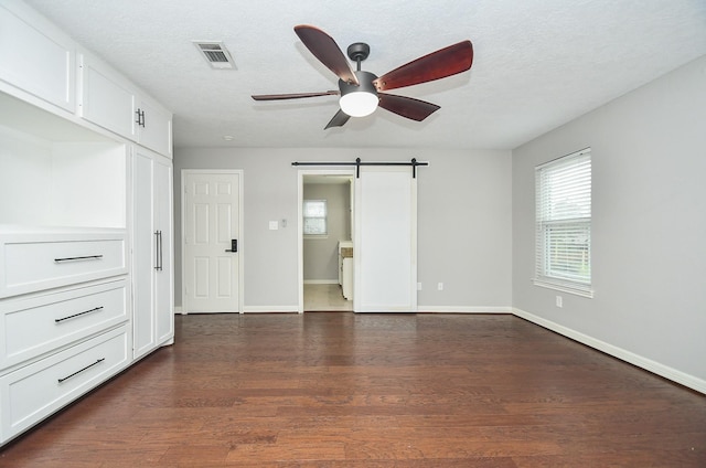 unfurnished bedroom featuring visible vents, a barn door, dark wood-type flooring, a textured ceiling, and baseboards