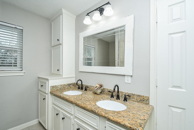 bathroom with double vanity, a sink, and baseboards