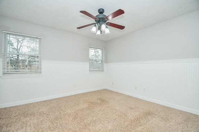 spare room with wainscoting, carpet flooring, and a ceiling fan