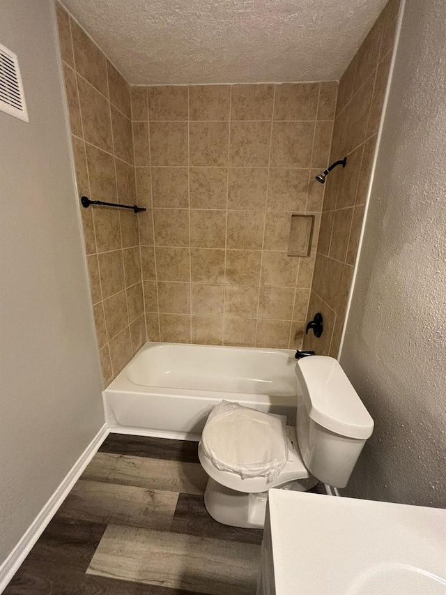 bathroom with toilet, tiled shower / bath combo, hardwood / wood-style floors, and a textured ceiling